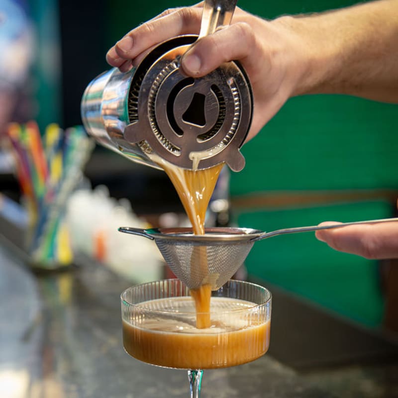 A cocktail being strained into a coupe at the bar